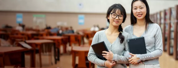 Two students holding books in a library